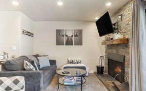 Ein Wohnzimmer mit Kamin, Wandfernseher und einer Couch mit Zierkissen.