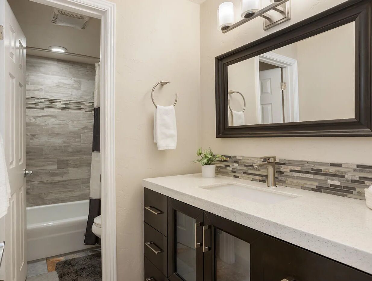 Un bagno con doccia, lavandino con specchio e porta asciugamani.