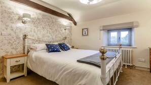Une chambre à coucher avec un lit, des tables de chevet, un radiateur, une fenêtre et un tableau au mur.