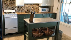 A kitchen with a stone backsplash, white cabinets, a stove, and a table with baskets.