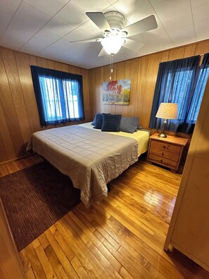 Ein Schlafzimmer mit einem Bett, einem Nachttisch, einer Lampe, einem Deckenventilator und Holzwänden.