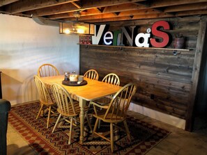 Ein Holzespeisetisch mit Stühlen, einem Teppich und einer Wand mit dem Text 'VernaS'.