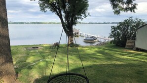 A backyard with a swing hanging from a tree, a dock extending into a lake, and a grassy lawn.