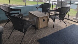 A covered patio with wicker furniture, a woven table, and a view of a lake.
