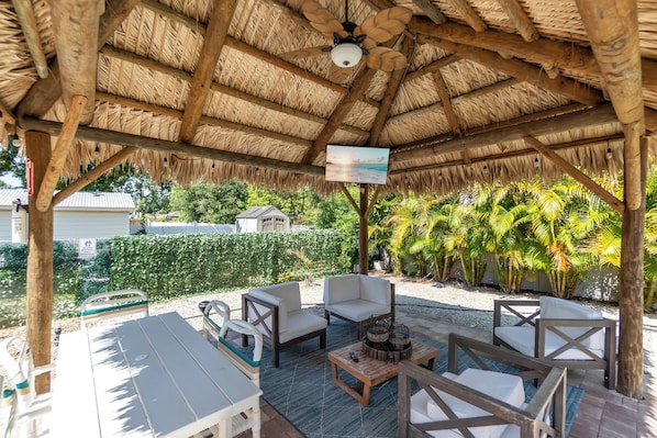 Une terrasse extérieure avec des meubles en bois, un ventilateur de plafond et un écran de télévision.