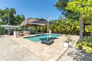 Une piscine dotée d’une structure de toit en chaume, entourée de palmiers et bordée d’une terrasse dallée.