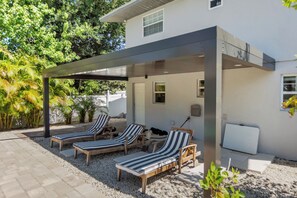 Et moderne hus med en overdækket patio, to liggestole og et lille bord.