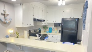 A kitchen with white cabinets, a black refrigerator, a coffee maker, and two bar stools with patterned cushions. - Let the fun begin 🏖🏊‍♀️😁<br>Located between both beaches (Rehoboth)