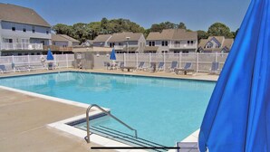 A swimming pool with lounge chairs and umbrellas, surrounded by a fence and houses in the background. - Let the fun begin 🏖🏊‍♀️😁<br>Located between both beaches (Rehoboth)