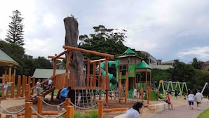 Un terrain de jeux avec des structures en bois, un toboggan et, au fond, un bâtiment vert.