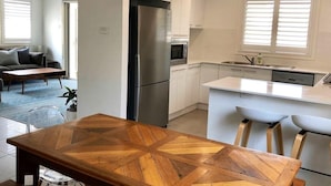 Une cuisine moderne avec des meubles blancs, un réfrigérateur en acier inoxydable et un petit îlot central doté de tabourets de bar.