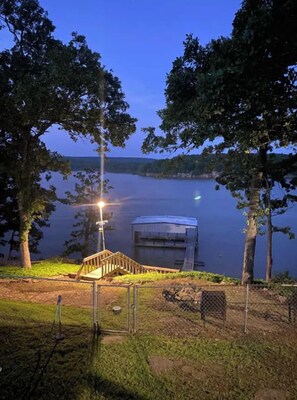 A dock extending into a calm lake at dusk, surrounded by trees and a grassy area.