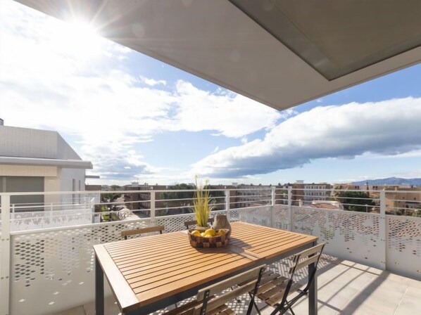 A balcony with a wooden table and chairs, a potted plant, and a bowl of lemons. - Alzina B by Interhome (Cambrils)