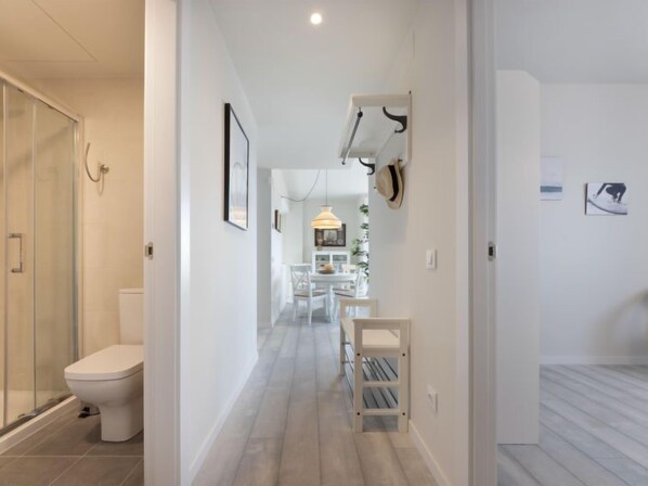A modern bathroom with a glass shower enclosure, a white toilet, and a hallway leading to a dining area with a table and chairs. - Alzina B by Interhome (Cambrils)