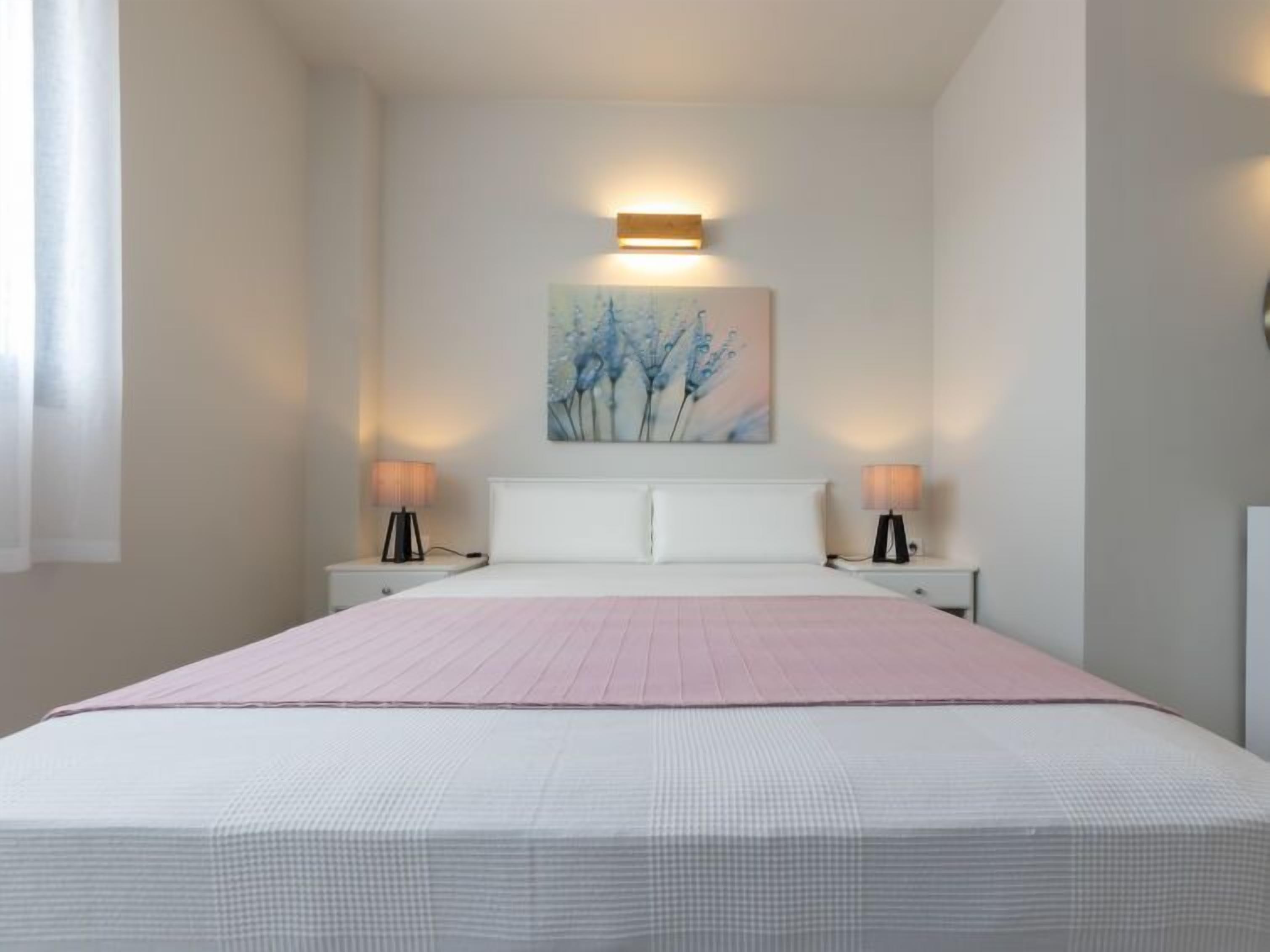 Une chambre à coucher bien rangée, avec un grand lit, deux tables de chevet et un luminaire fixé au mur.
