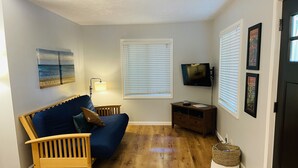 Un salon avec un canapé bleu, un plancher en bois, un téléviseur fixé au mur et des tableaux encadrés.