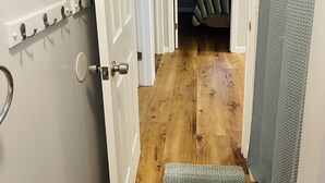 Un couloir avec un plancher en bois, une porte dotée d’une poignée en métal, un interrupteur fixé au mur et un tableau encadré.