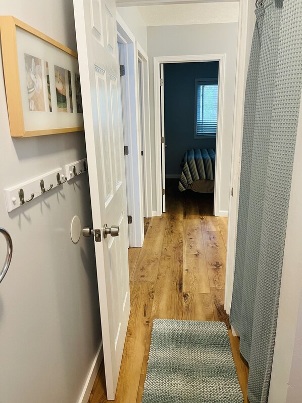 A hallway with a wooden floor, a door with a metal handle, a wall-mounted light switch, and a framed picture.