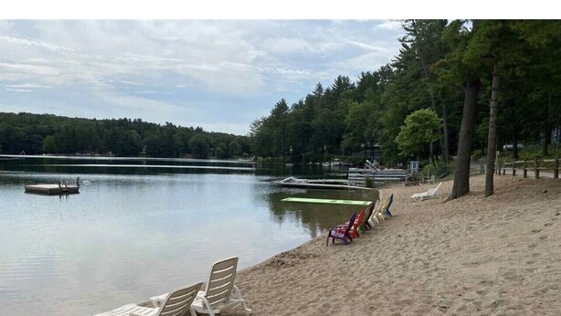 Une plage au bord d’un lac, avec des chaises longues blanches et un quai.