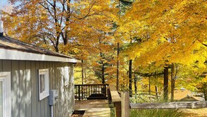 Une terrasse en bois mène à un chalet doté d’un porche abrité, le tout entouré d’arbres aux feuilles d’automne.