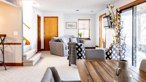 A modern living room with a wooden table, grey sofas, and a staircase leading to another level. - Stunning Lake Front Home - Zero Entry Water Access (Sunrise Beach)