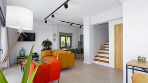 Una sala de estar moderna con un sofá, una mesa de centro y un televisor. Se ve una escalera que sube a otro nivel.