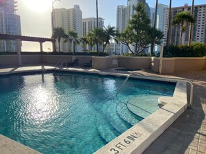 A swimming pool with a 3ft 6in depth marker, surrounded by palm trees and buildings in the background.