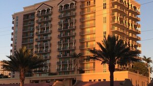Un hotel de varios pisos con balcones, palmeras y un cielo despejado.