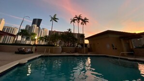 Una piscina con vistas a la puesta de sol, palmeras y edificios altos al fondo.