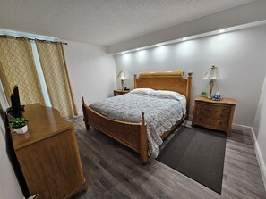 A bedroom with a wooden bed, two bedside tables with lamps, a wooden dresser, and a dark rug.