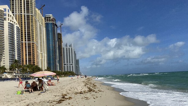Una playa con edificios altos al fondo, orilla arenosa y olas del océano.