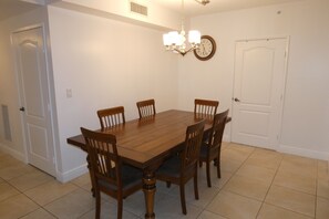 A dining room with a wooden table and six chairs, a chandelier, a clock, and a white door.