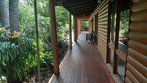 Eine Holzterrasse mit überdachtem Gang, der zu einem Gebäude führt, umgeben von dichtem Grün.