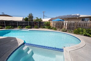 Una piscina con borde curvo y detalle de azulejos azules, rodeada por una valla de madera y follaje.
