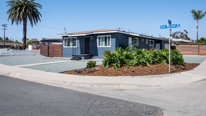 A single-story house with a dark blue exterior, a small front porch, and a well-maintained garden with various plants. - Beautiful house close to San Diego Zoo, Sea World, Coronado (Chula Vista)