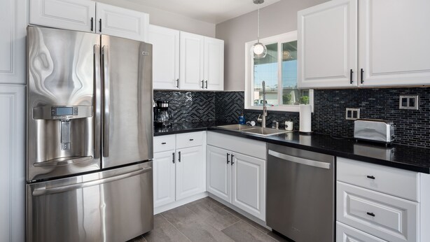 A modern kitchen with stainless steel appliances, white cabinetry, and a black backsplash. - Beautiful house close to San Diego Zoo, Sea World, Coronado (Chula Vista)