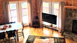 A cozy cabin interior with wooden walls, a stone fireplace, a large TV, and a dining area with a table and chairs. - Welcome to LAZY DEER CABIN! (Piney Creek)