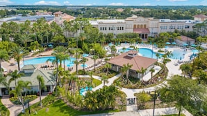 Un complexe hôtelier doté de plusieurs piscines, de palmiers et d’un grand bâtiment surmonté d’un toit recouvert de tuiles rouges.
