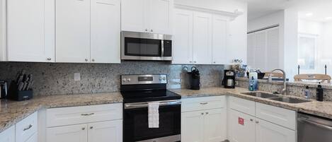 A modern kitchen with white cabinets, stainless steel appliances, granite countertops, and a built-in oven.