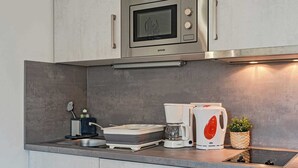 Une cuisine moderne équipée d’un four à micro-ondes encastré, d’une machine à café et d’une bouilloire posées sur le plan de travail.