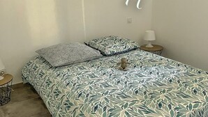 A bedroom with a bed, pillows, a bedside table, and a lamp. - 40m2 T2 apartment Small medieval village in the heart of the Roussillon vineyards (Baixas)