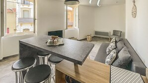 A modern kitchen with a central island, bar stools, and a hanging light fixture. - 40m2 T2 apartment Small medieval village in the heart of the Roussillon vineyards (Baixas)