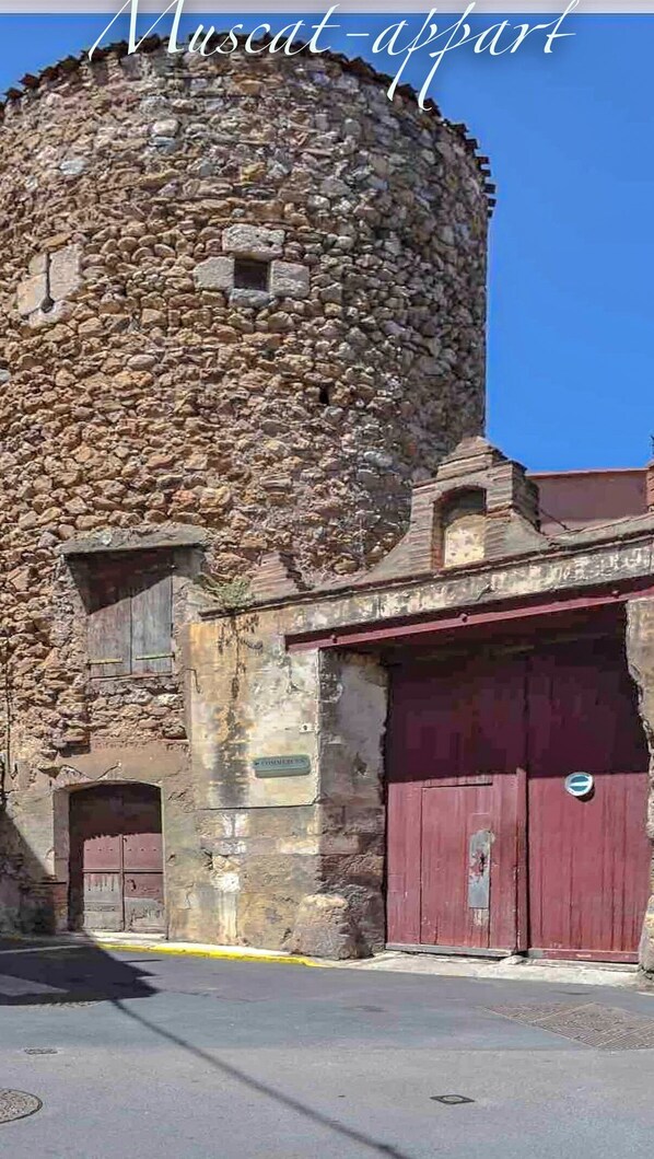 Un bâtiment historique en pierre, doté d’une tour cylindrique, d’une porte rouge et d’une petite fenêtre.