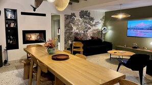 Uma sala de estar moderna com uma mesa de jantar de madeira, lareira, televisão grande e uma parede decorativa com árvores artificiais.
