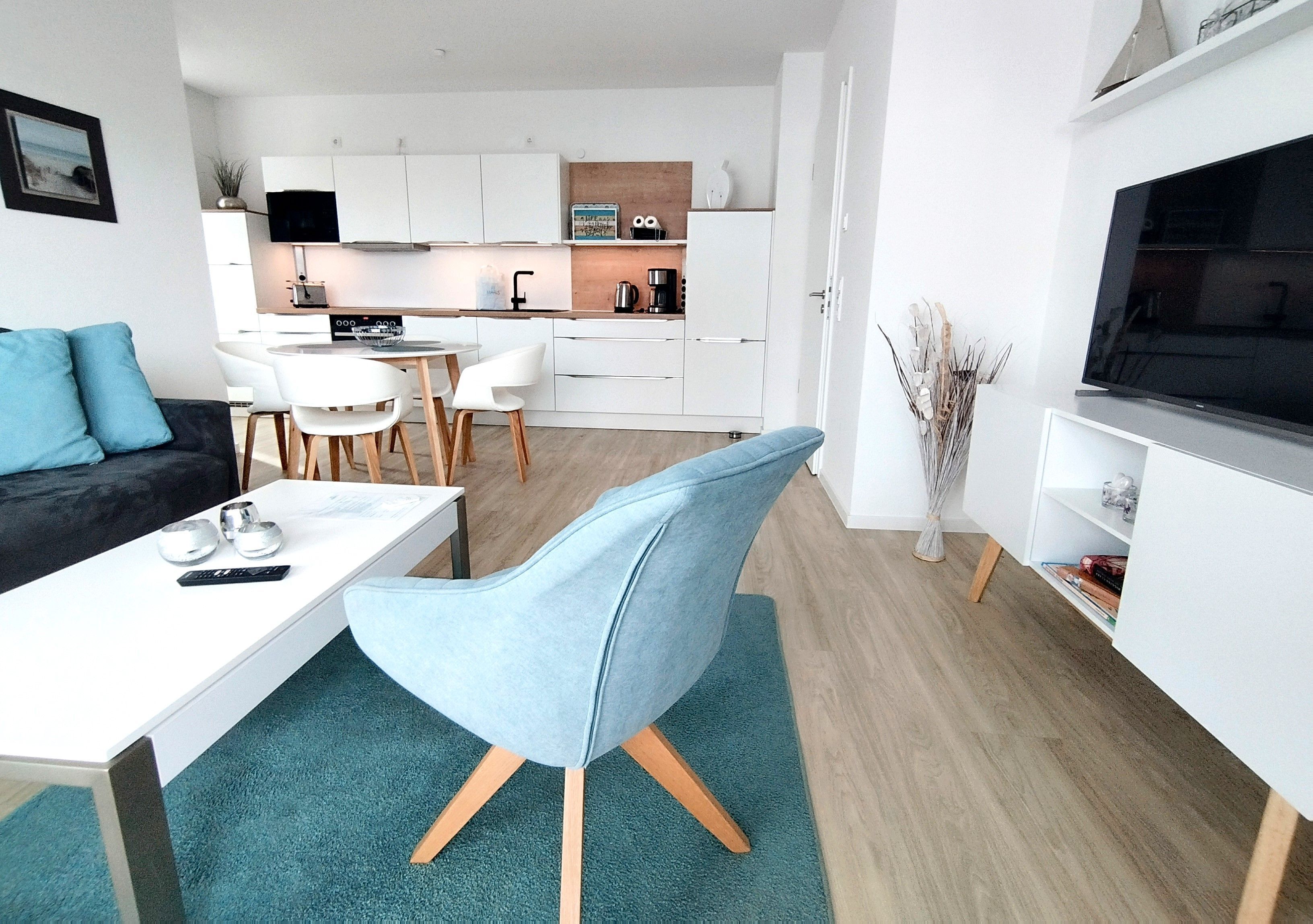 Een moderne woonkamer met een bank, een salontafel, een televisie en een keuken met witte kasten en een eettafel.