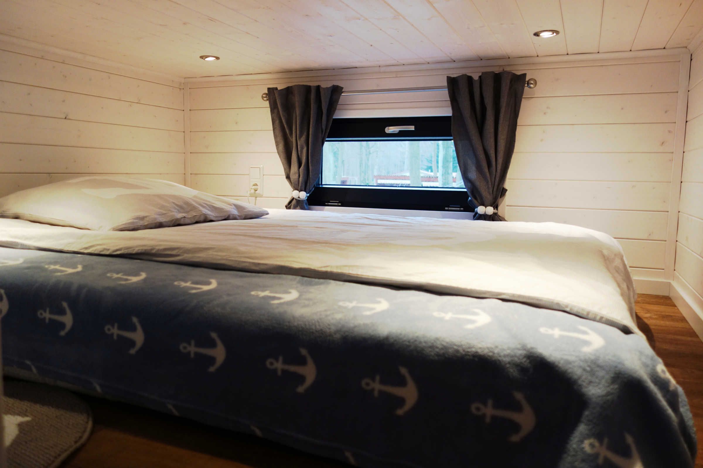 A bedroom with a bed, curtains, a window, and wooden walls.