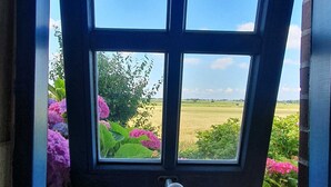 A window with a view of a field and flowers. - Kapitänshuus, Deutschland (Nordstrand)