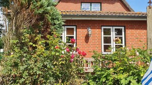 A traditional brick house with a thatched roof, white window frames, and a small garden with blooming flowers. - Kapitänshuus, Deutschland (Nordstrand)