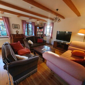 A cozy living room with wooden beams, a fireplace, a bookshelf, and a television.