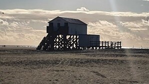 Ett hus vid stranden med en stor terrass och ett litet förråd.
